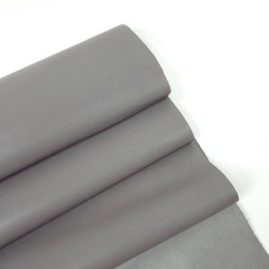 Puede incluir: Un trozo de tela de cuero gris doblado. El cuero es liso y tiene un ligero brillo.