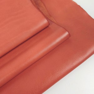 May include: A stack of four pieces of red leather. The leather is smooth and has a slight sheen.