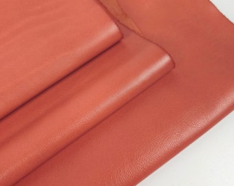 May include: A stack of four pieces of red leather. The leather is smooth and has a slight sheen.