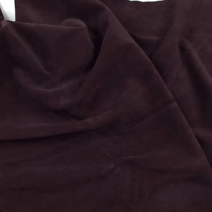 May include: A length of dark burgundy fabric, possibly suede or leather, is draped and folded. The material has a soft, matte appearance and a rich, deep colour. The folds create shadows and highlights, adding depth to the textile. The fabric is likely used for apparel or crafting.