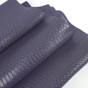 May include: A folded sheet of dark purple material featuring a raised, embossed texture that mimics the appearance of snake scales. The surface has a matte finish with a repeating pattern of small, irregular shapes across the entire piece.