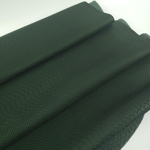 Puede incluir: Una hoja de material de color verde bosque oscuro con una textura en relieve que imita la piel de serpiente. La superficie muestra un patrón repetitivo de pequeñas formas similares a escamas en toda el área visible, con pliegues que crean profundidad y sombras.