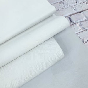 Könnte beinhalten: Nahaufnahme von weißen Lederblättern mit unterschiedlichen Texturen. Das obere Blatt ist glatt, während das mittlere Blatt ein subtiles, strukturiertes Muster aufweist. Das untere Blatt ist ein hellerer Weißton und hat eine glatte Oberfläche.