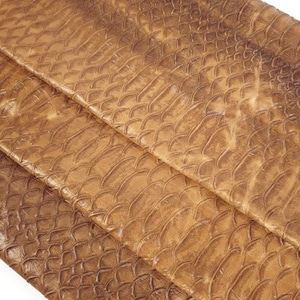 May include: Close-up of a brown faux snakeskin fabric with a textured pattern. The fabric is folded in thirds, showing the pattern from different angles.