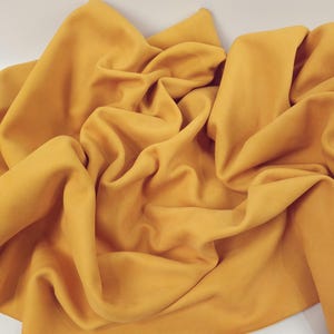 Pode incluir: Um pedaço de tecido amarelo mostarda amassado. O tecido é macio e tem uma textura lisa.