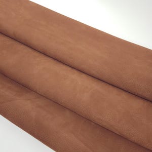Op de afbeelding: Close-up van verschillende lagen bruin leer. Het leer heeft een textuur met kleine, gelijkmatig verdeelde bobbels. De kleur is een warm, aards bruin en het leer lijkt zacht en soepel.