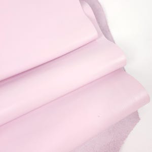 Peut inclure: Gros plan sur trois feuilles de cuir rose clair. Les deux feuilles supérieures sont pliées, révélant le dessous rugueux et non fini du cuir. Le cuir a une finition lisse et mate et une couleur pastel douce.