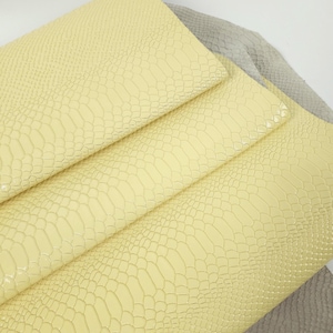 May include: Close-up of a stack of yellow faux leather with a crocodile skin pattern. The leather is smooth and shiny.