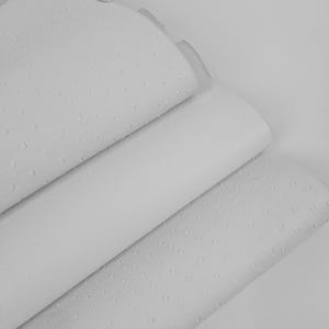 Puede incluir: Una pila de tres hojas de cuero blanco que presenta una textura distintiva de estilo avestruz con pequeñas protuberancias elevadas y espaciadas uniformemente por toda la superficie. El material tiene un acabado mate y está superpuesto.