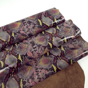 May include: Close-up of a folded piece of fabric with a snakeskin pattern in shades of pink, yellow, and black. The fabric is folded on top of a brown piece of fabric.