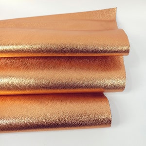 May include: A close-up of a folded piece of metallic copper-colored leather. The leather has a textured surface.