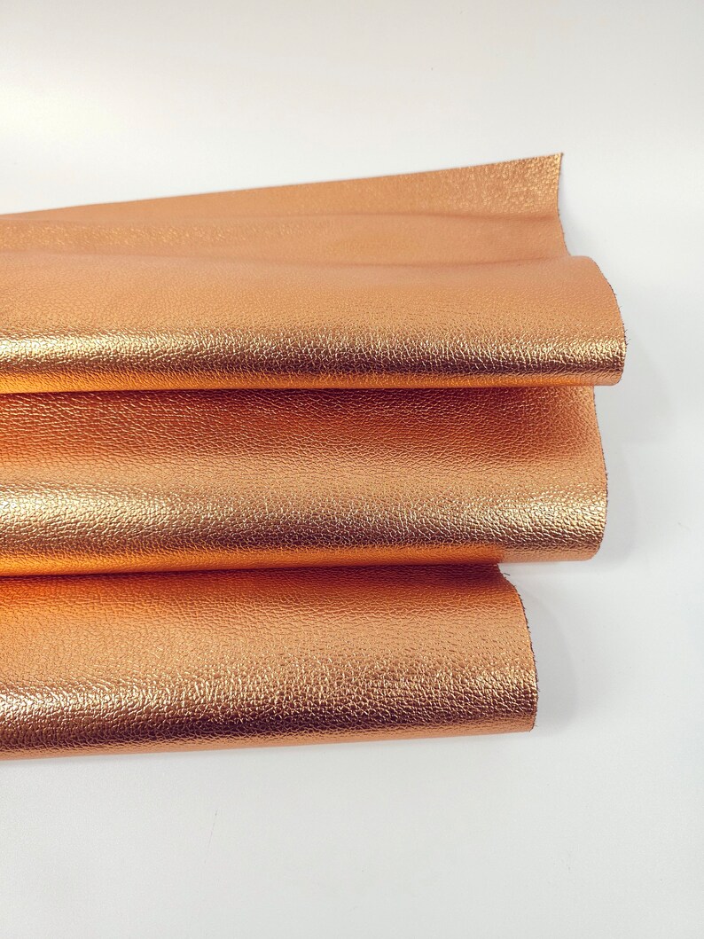 May include: A close-up of a folded piece of metallic copper-colored leather. The leather has a textured surface.