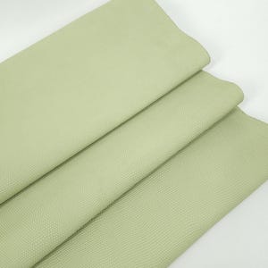 May include: Close-up of three folded sheets of light green textured leather. The leather has a subtle, repeating pattern and a matte finish. The text "Leatherforcraft" is visible in the bottom left corner.