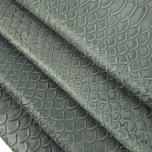 Könnte beinhalten: Grauer, strukturierter Stoff mit einem Schuppenmuster. Der Stoff ist dreifach gefaltet und zeigt das Muster aus verschiedenen Blickwinkeln.