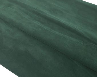 May include: A close-up shot of a folded piece of dark green fabric. The fabric has a soft, velvety texture and appears to be draped. The folds create shadows and highlights, adding depth to the image. The color is a deep, rich shade of green.