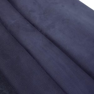 Pode incluir: Um pedaço de couro roxo escuro com uma textura de grão visível. O material está dobrado sobre si mesmo, criando sombras e reflexos diagonais profundos na superfície, exibindo o acabamento fosco e o padrão natural e irregular da pele.