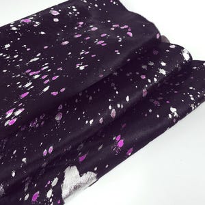 May include: Black cowhide leather with a speckled design in silver and pink. The leather is folded, showing the texture and pattern. The design is a splatter effect, creating a unique look.