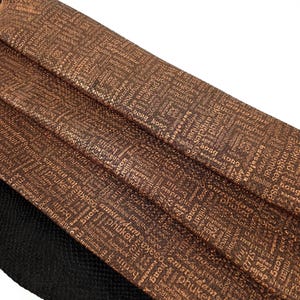 Op de afbeelding: Bruin leer met een textuur en een patroon van in goud gedrukte stadsnamen. Het leer is in drieën gevouwen.