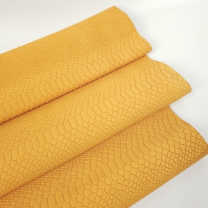 Puede incluir: Primer plano de una tela de imitación de cuero amarilla con un patrón de piel de serpiente.