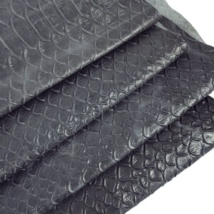 Könnte beinhalten: Nahaufnahme von dunkelgrauem Schlangenleder. Das Leder ist in mehreren Schichten gefaltet, wodurch die Textur und das Muster der Schuppen sichtbar werden.