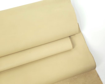 May include: A close-up of a beige leather hide, partially rolled and folded. The leather has a smooth, finished surface on one side and a rough, suede-like texture on the other. The colour is a warm, neutral tone.