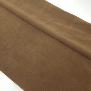 May include: A folded length of brown fabric, displaying a soft, suede-like texture. The material has a warm, earthy tone, with subtle colour variations and slight creases.