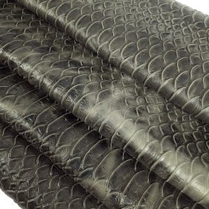 Könnte beinhalten: Nahaufnahme eines gefalteten Stücks grauen Schlangenleders mit einem strukturierten, schuppigen Muster.