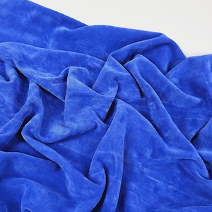 Könnte beinhalten: Nahaufnahme eines leuchtend blauen Stoffes mit weicher, samtiger Textur. Der Stoff ist drapiert und gefaltet, wodurch Schatten und Lichtreflexe entstehen, die sein weiches Aussehen betonen. Die Farbe ist ein sattes, gesättigtes Blau.