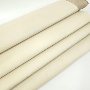 May include: A close-up of a stack of off-white leather sheets with a textured surface. The leather is folded over itself, revealing the underside of the material.