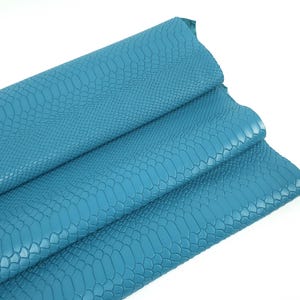 Könnte beinhalten: Tealblauer Kunstleder mit einem Schlangenhautprägemuster. Das Leder ist dreifach gefaltet.