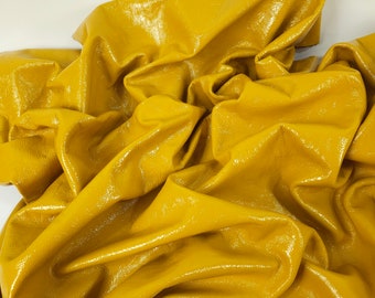 May include: A close-up of a crumpled piece of yellow leather. The leather has a glossy finish and is folded in a way that shows its texture.