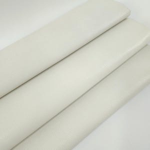 May include: A close-up of a stack of white faux leather fabric with a textured, pebbled surface.