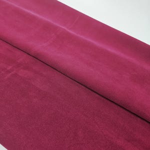Può includere: Primo piano di un pezzo di tessuto bordeaux piegato. Il tessuto ha una consistenza morbida e vellutata e un colore ricco e intenso. Il materiale è probabilmente utilizzato per abbigliamento, tappezzeria o progetti artigianali.