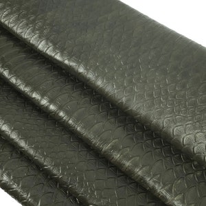Puede incluir: Primer plano de una tela de cuero verde oscuro con un patrón texturizado escamoso. La tela está doblada en tres partes, revelando la textura.
