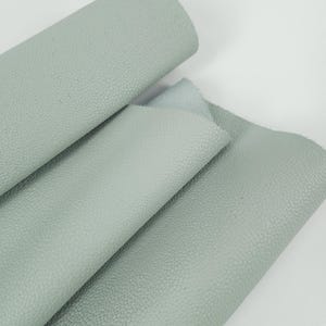 May include: Close-up of several sheets of light blue leather. The leather has a textured, bumpy surface. One sheet is rolled up, while the others are folded and layered, revealing the material's texture and color variations.