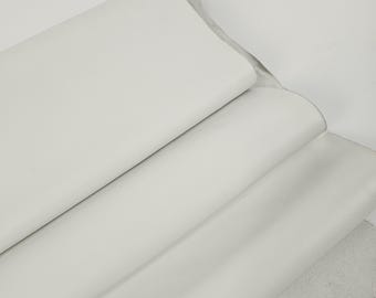May include: A close-up shot of several rolls of white leather. The leather is smooth and appears to be of high quality. The rolls are stacked on top of each other, with the edges of the leather visible. The background is a plain white.