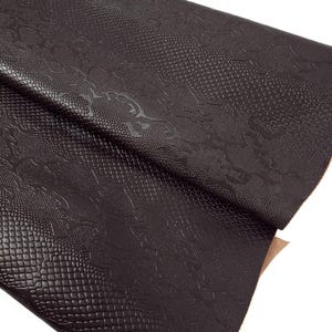 Könnte beinhalten: Ein dunkelbraunes Kunstlederblatt mit einem Schlangenhautprägemuster.