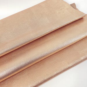May include: A stack of three sheets of rose gold faux leather with a textured, snake-like pattern.