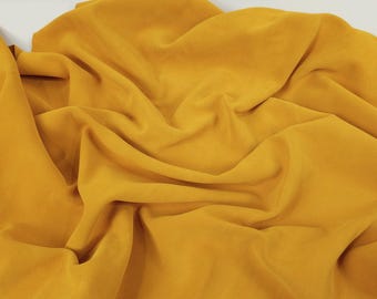 May include: A close-up of a crumpled piece of mustard yellow fabric. The fabric has a smooth, silky texture.