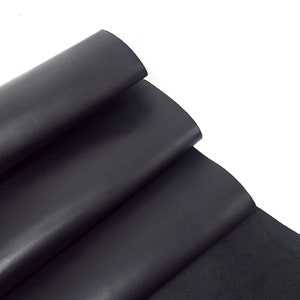 Peut inclure: Gros plan sur plusieurs feuilles de cuir noir. Le cuir a une surface lisse et brillante et est plié sur lui-même. Les bords du cuir sont visibles, révélant l'épaisseur et la texture du matériau. Le fond est blanc.