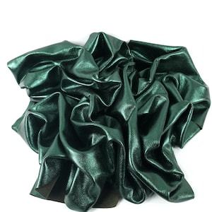 Puede incluir: Una tela de cuero metálico verde oscuro con un acabado liso y brillante. La tela está arrugada y doblada, mostrando su textura y caída.