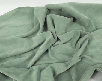 May include: A piece of soft, sage green fabric folded on a white surface. The fabric has a slightly textured surface.