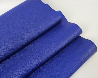 May include: A stack of vibrant blue leather sheets. The leather has a textured surface and is folded over itself, revealing the edges of the material. The color is a deep, saturated blue, and the material appears to be soft and pliable.