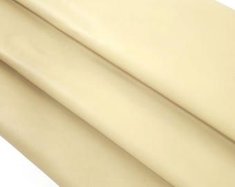 May include: Close-up of a stack of beige leather sheets. The leather has a smooth, matte finish and appears to be folded over itself. The colour is a light, neutral tone, suitable for various crafting projects.