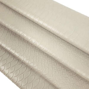 Könnte beinhalten: Nahaufnahme eines hellbeigen Kunstleders mit einem strukturierten, schuppigen Muster. Der Stoff ist in mehreren Schichten gefaltet, wodurch die Textur hervorgehoben wird.