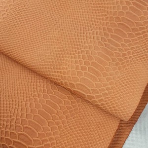 May include: A close-up of a piece of orange faux leather with a snakeskin pattern.