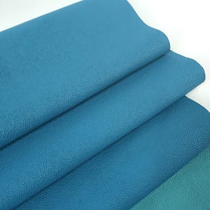 May include: A stack of teal blue leather sheets with a textured surface. Leatherforcraft is printed on the bottom sheet.