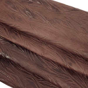 Puede incluir: Primer plano de una tela de cuero marrón con un patrón de plumas texturizado.