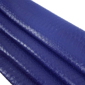 Könnte beinhalten: Nahaufnahme eines blauen Kunstleders mit einer strukturierten, schuppigen Textur. Der Stoff ist gefaltet und drapiert, wodurch die Textur und Farbe sichtbar werden.