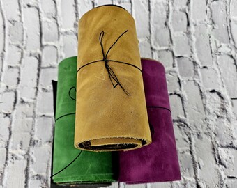 May include: Three rolls of leather in different colours: green, brown, and purple. The leather is rolled up and tied with a black string.